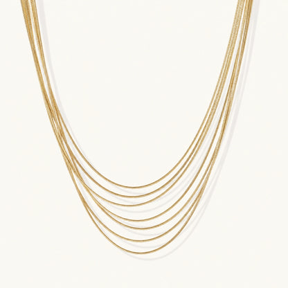 Seven delicate gold-plated snake chains create an elegant layered necklace on a neutral background.